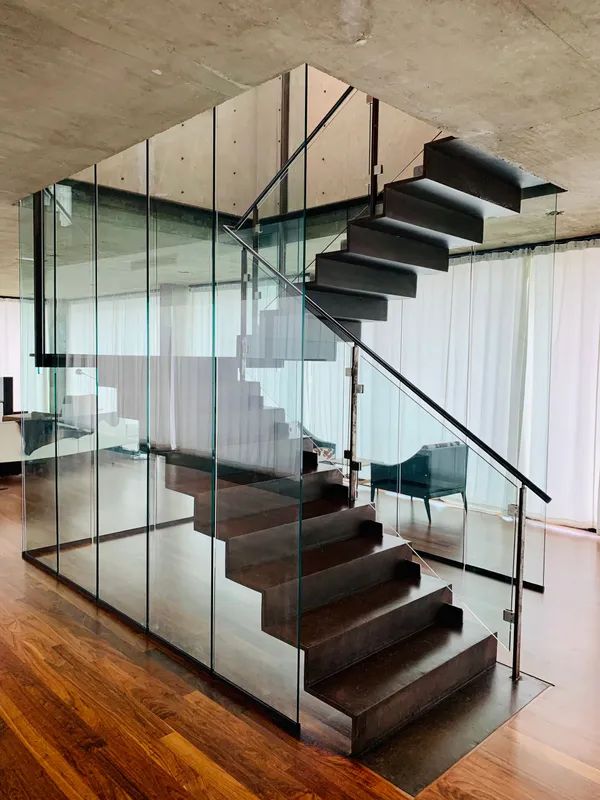 Modern staircase with dark wood steps and glass walls. Silver railing and hardwood floor.