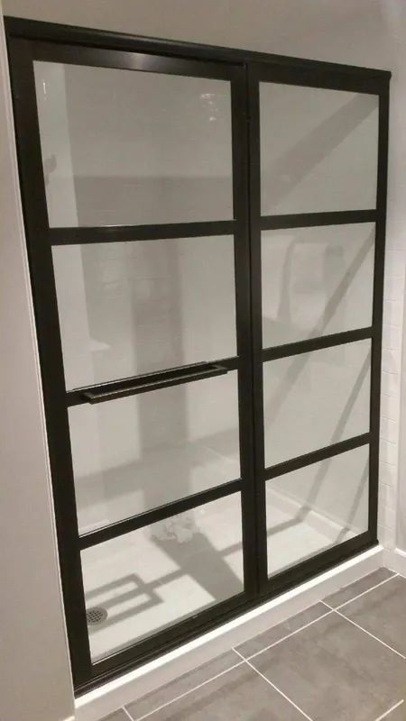 Dark-framed shower enclosure with multiple glass panes. Interior bathroom shot with tiled floor.