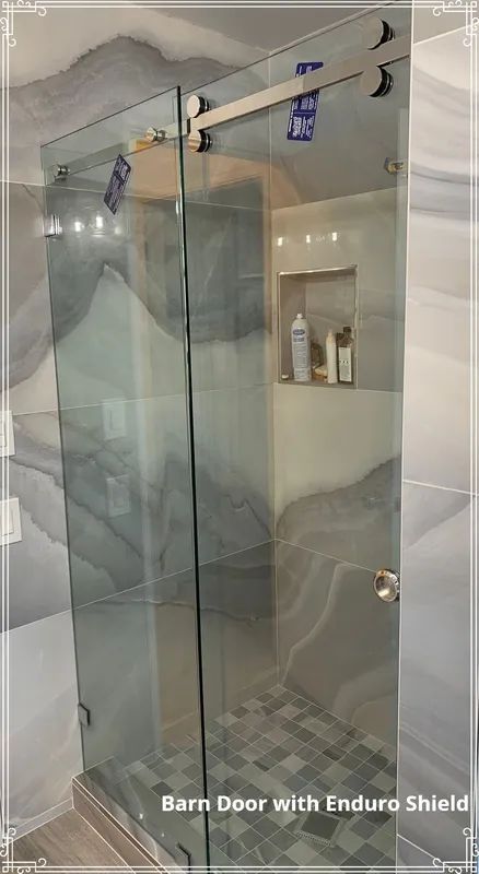 Glass shower door, barn door style, in bathroom with gray stone-look tile.