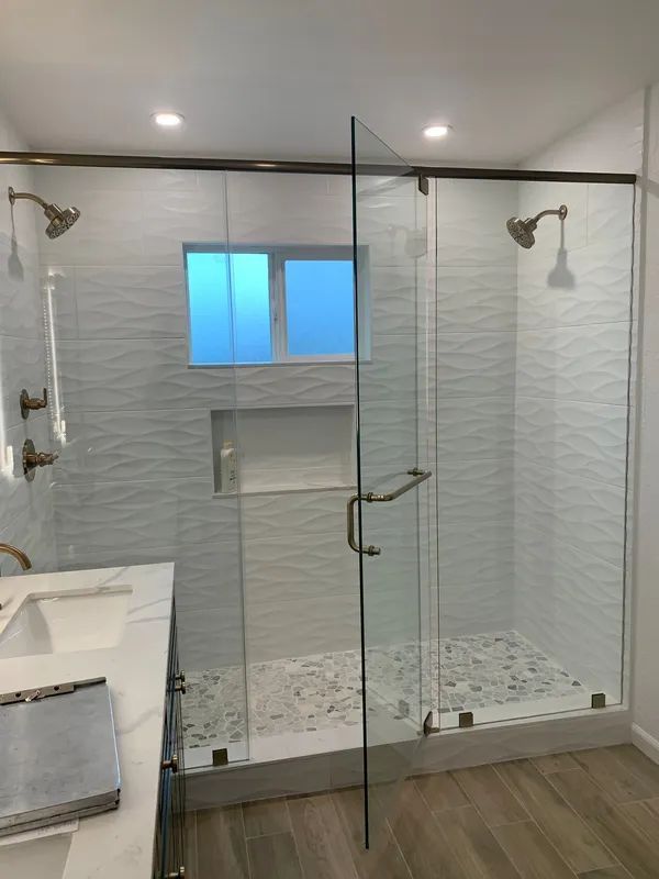 Bathroom with a glass shower enclosure, white textured tile, pebble shower floor, and brushed bronze fixtures.