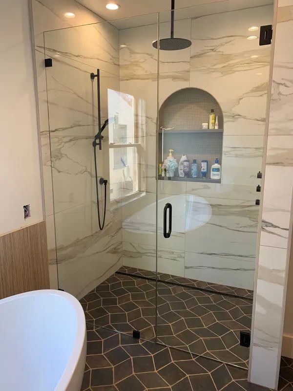 Bathroom with glass shower, marble tile, and dark floor tiles. Black shower fixtures and handle.