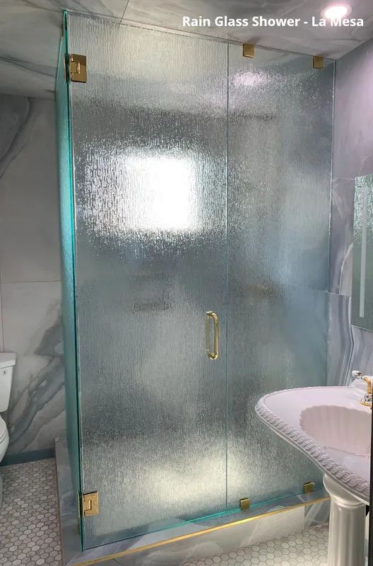 Rain glass shower enclosure with gold hardware in a bathroom.