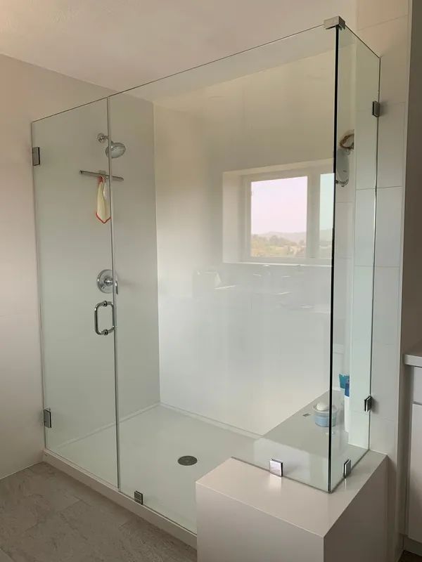 Glass shower enclosure with white walls, a window, and a white shower basin.