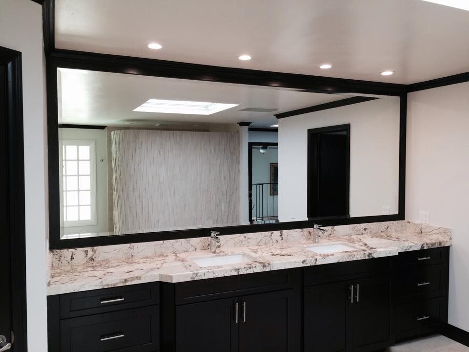 Bathroom with a large mirror above a granite countertop with three sinks and dark cabinets.