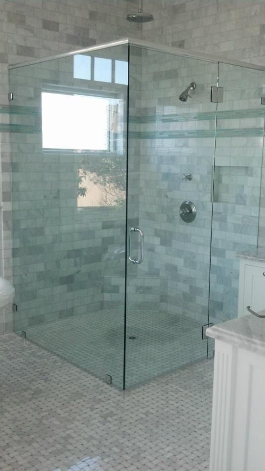 Corner glass shower enclosure in a bathroom with tiled walls and floor.