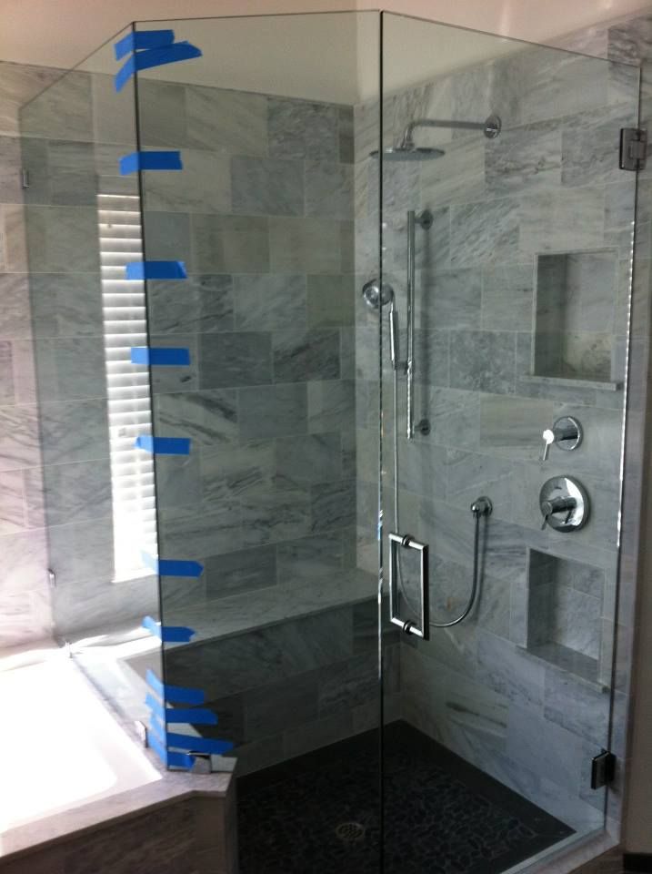 Glass shower enclosure with gray tiled walls and black tiled floor.