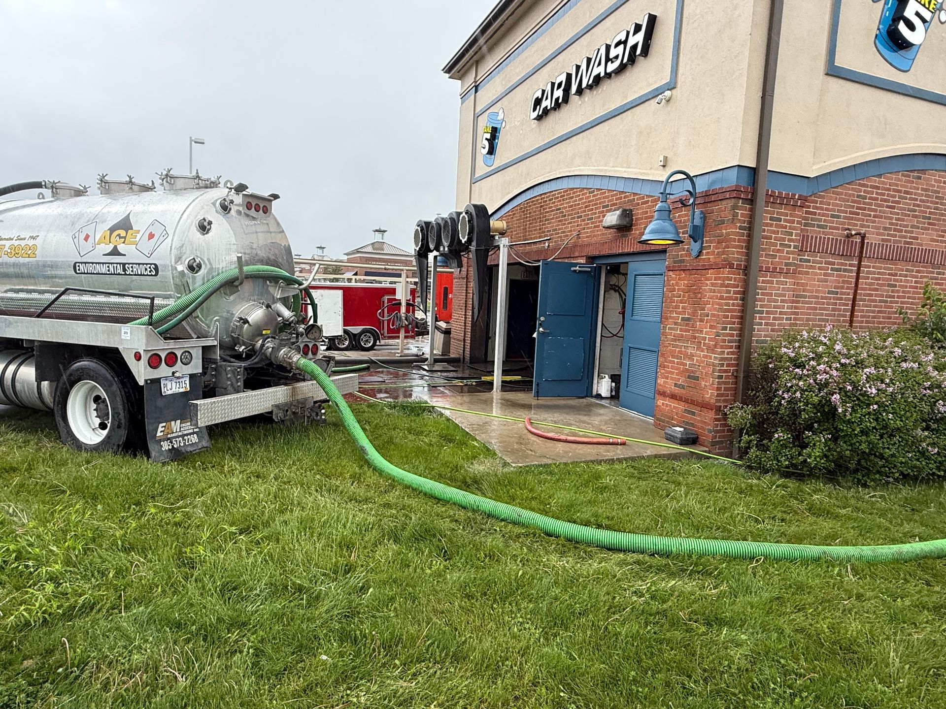 Vacuum truck pumping green hose into a building’s side entrance at a car wash