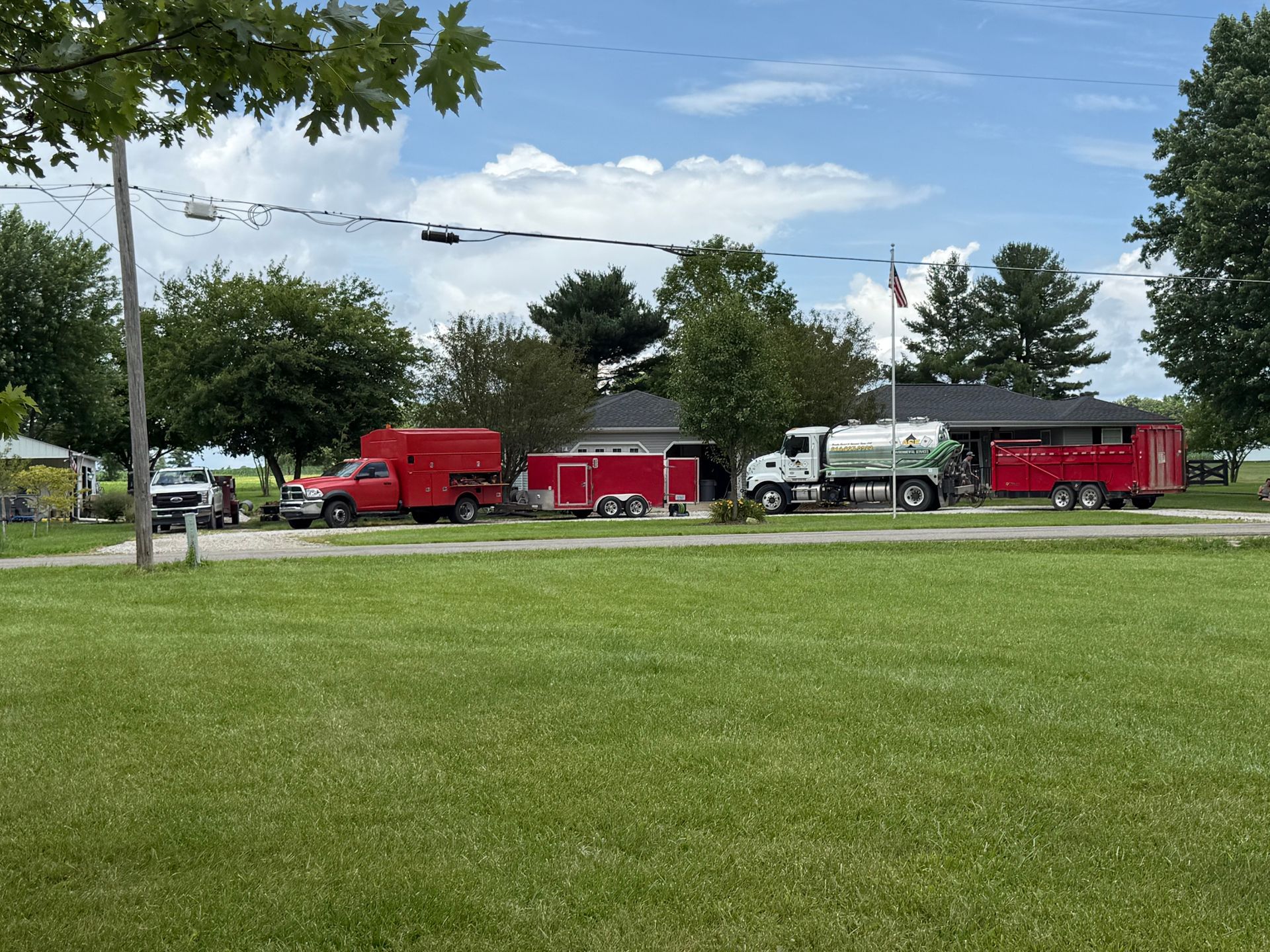 Red emergency trucks parked on a grassy roadside beneath cloudy sky, with trees and power lines nearby