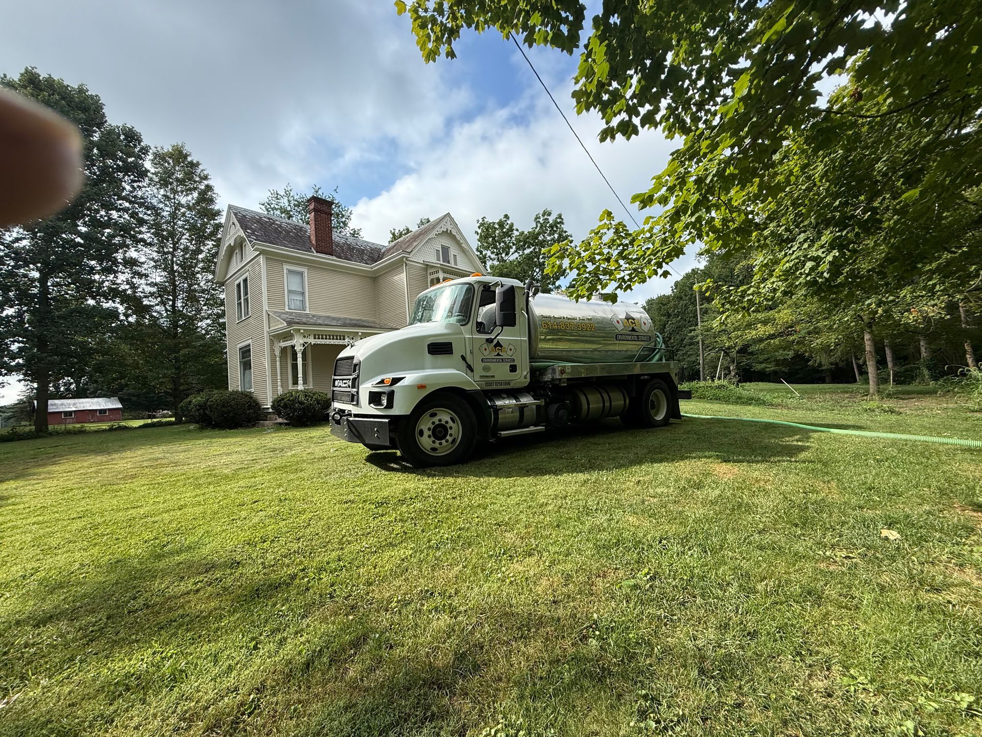 White dump truck parked on grass beside a house under trees on a sunny day
