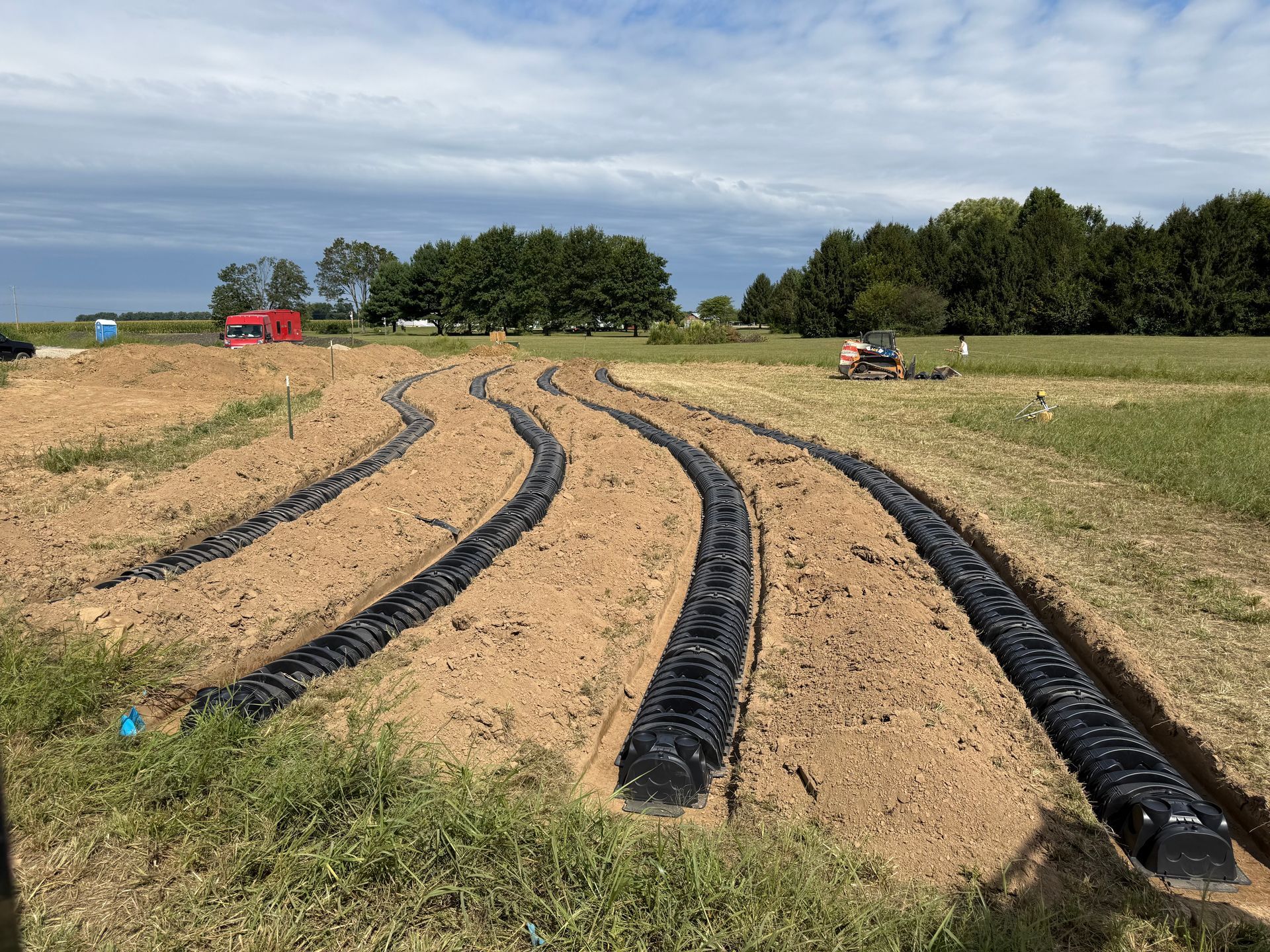 Curved black irrigation tubing laid across a sandy field under a cloudy sky.