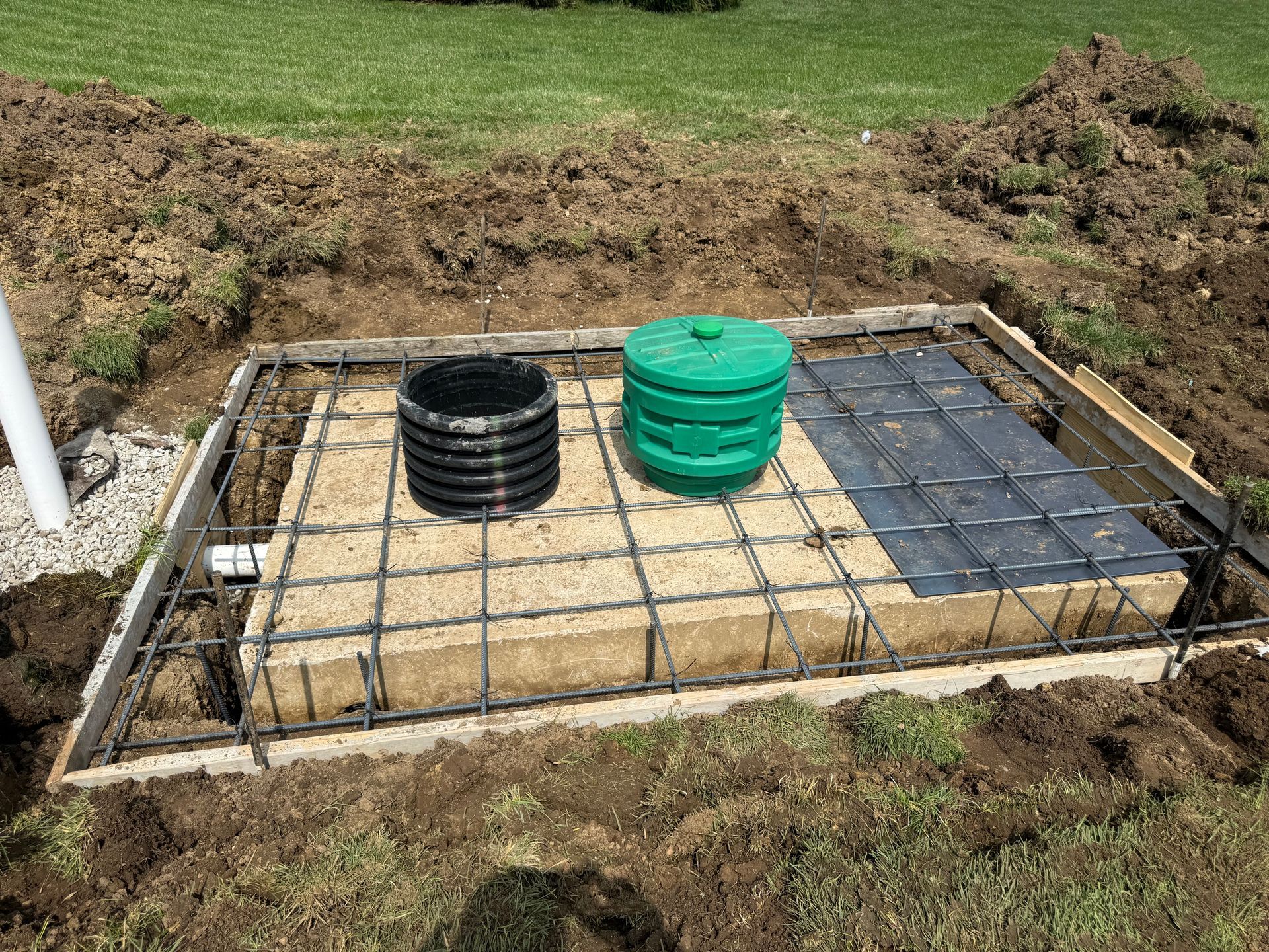 Construction site with rebar foundation, black and green buckets, and concrete blocks in a dug-out area