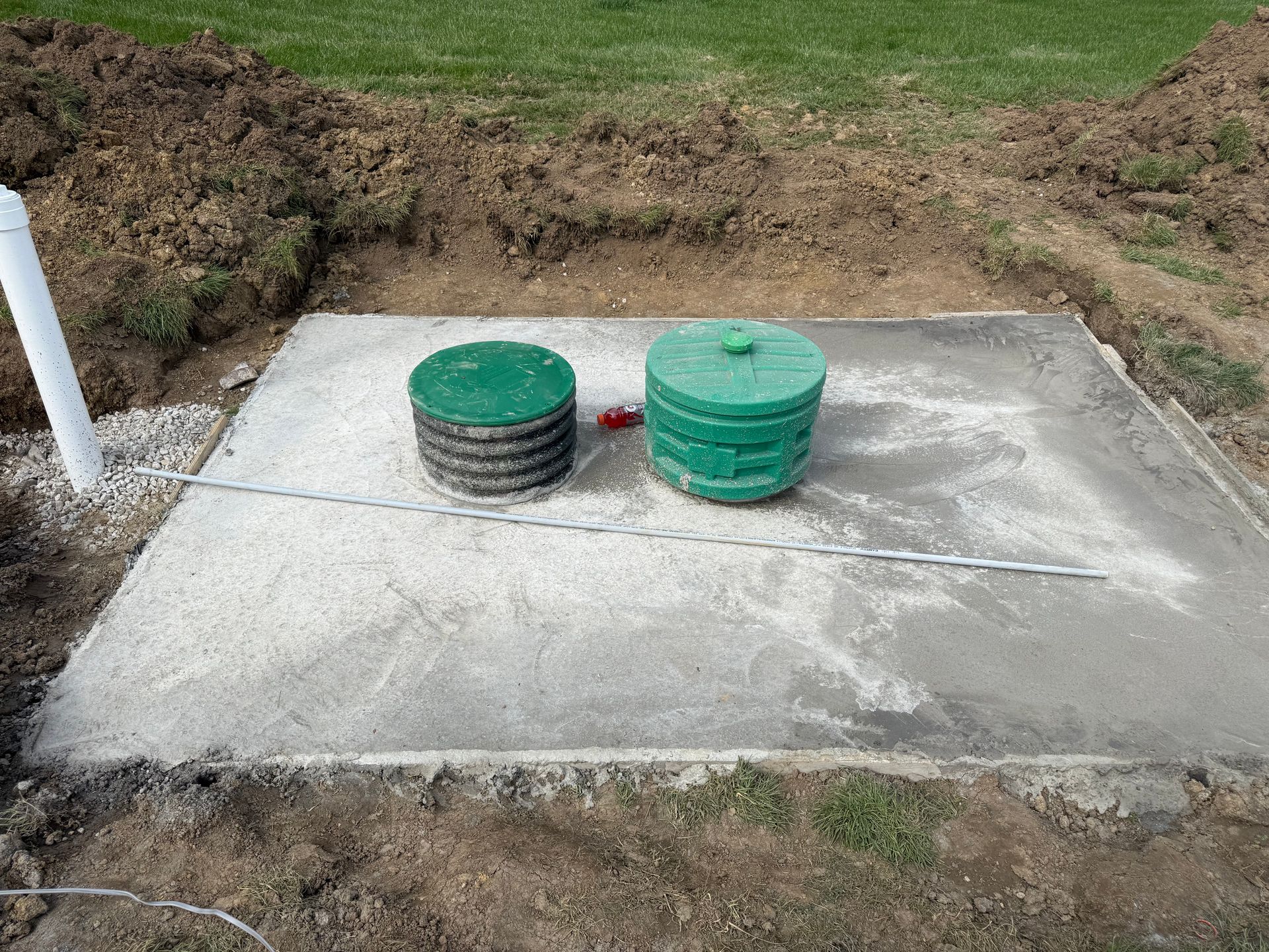 Two green utility covers on a concrete slab beside a grassy ditch