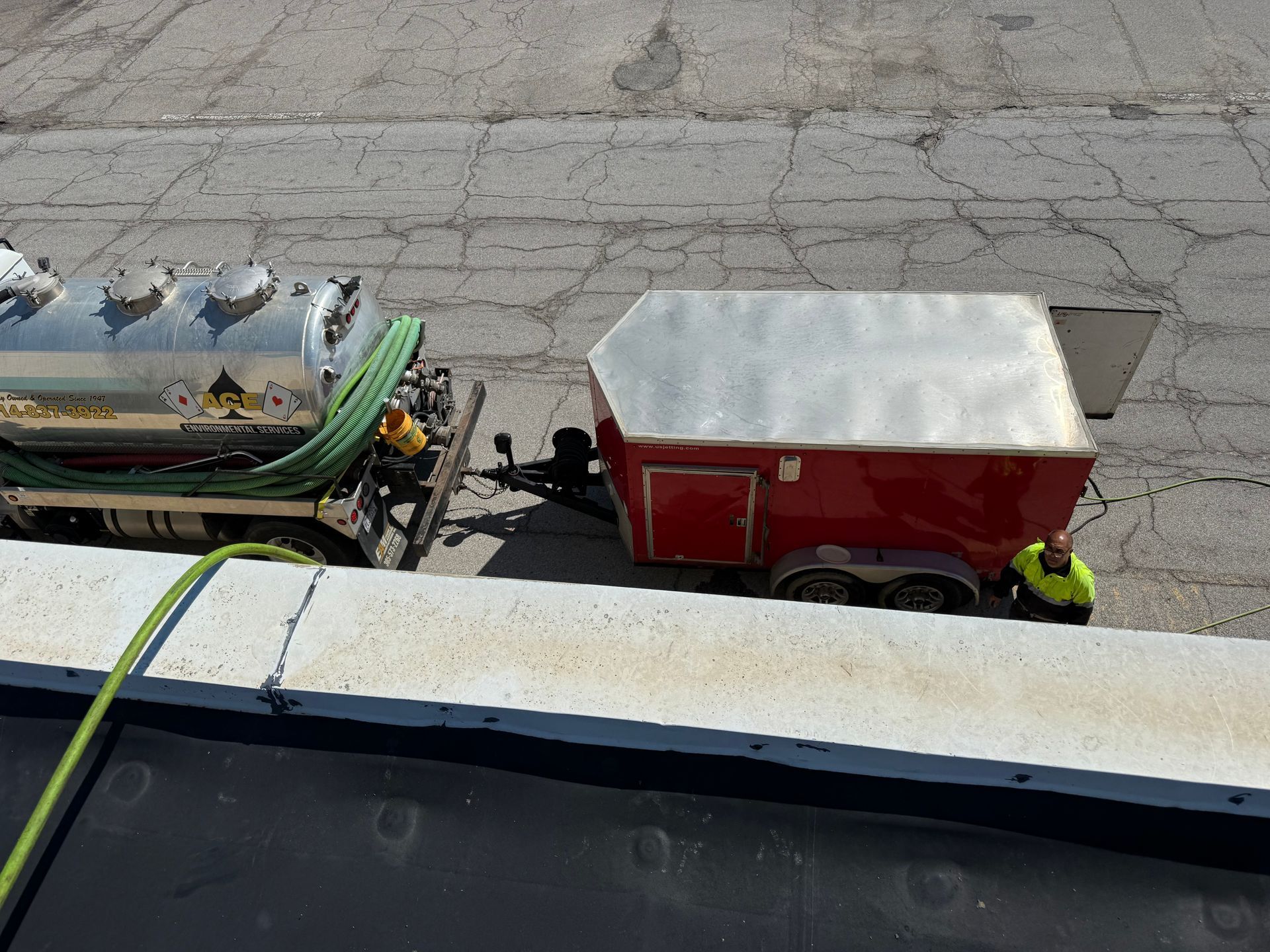 Two small trailers parked on cracked pavement, one red with a white cover and a worker in a neon vest nearby