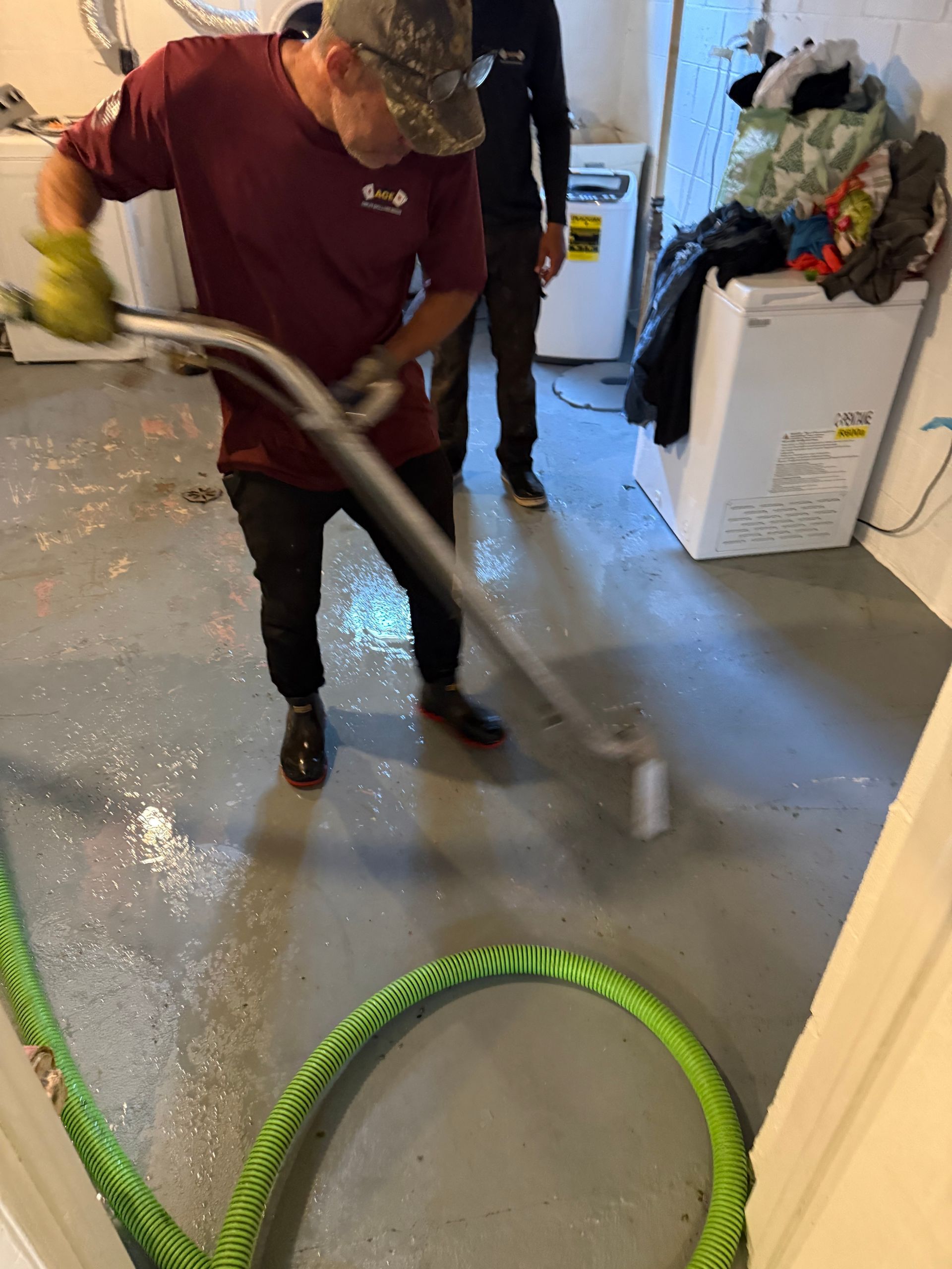 Worker vacuuming water from a hallway floor with a wet vacuum and hose.
