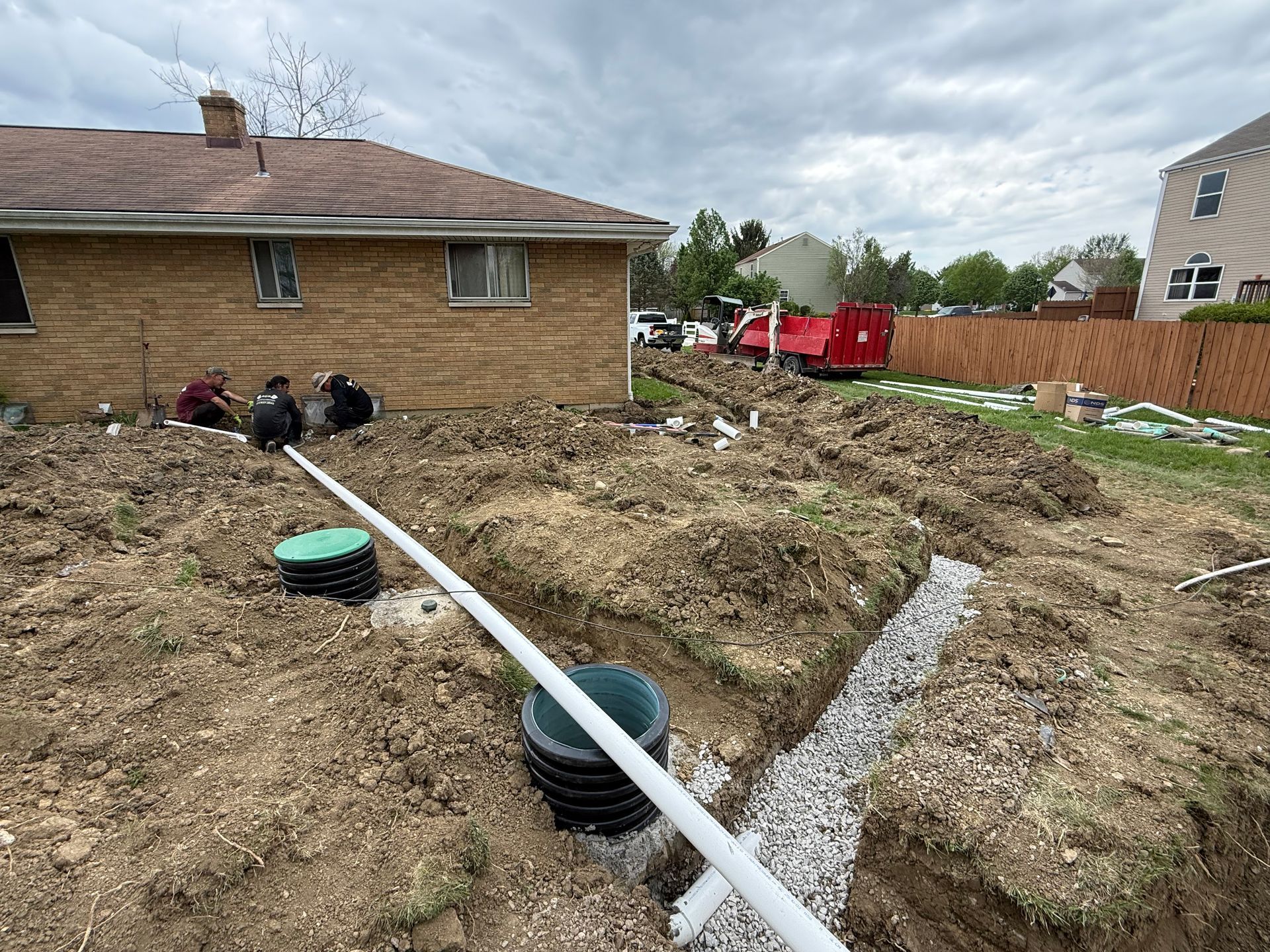 Backyard excavation with trenches, PVC pipes, and utility boxes beside a brick house