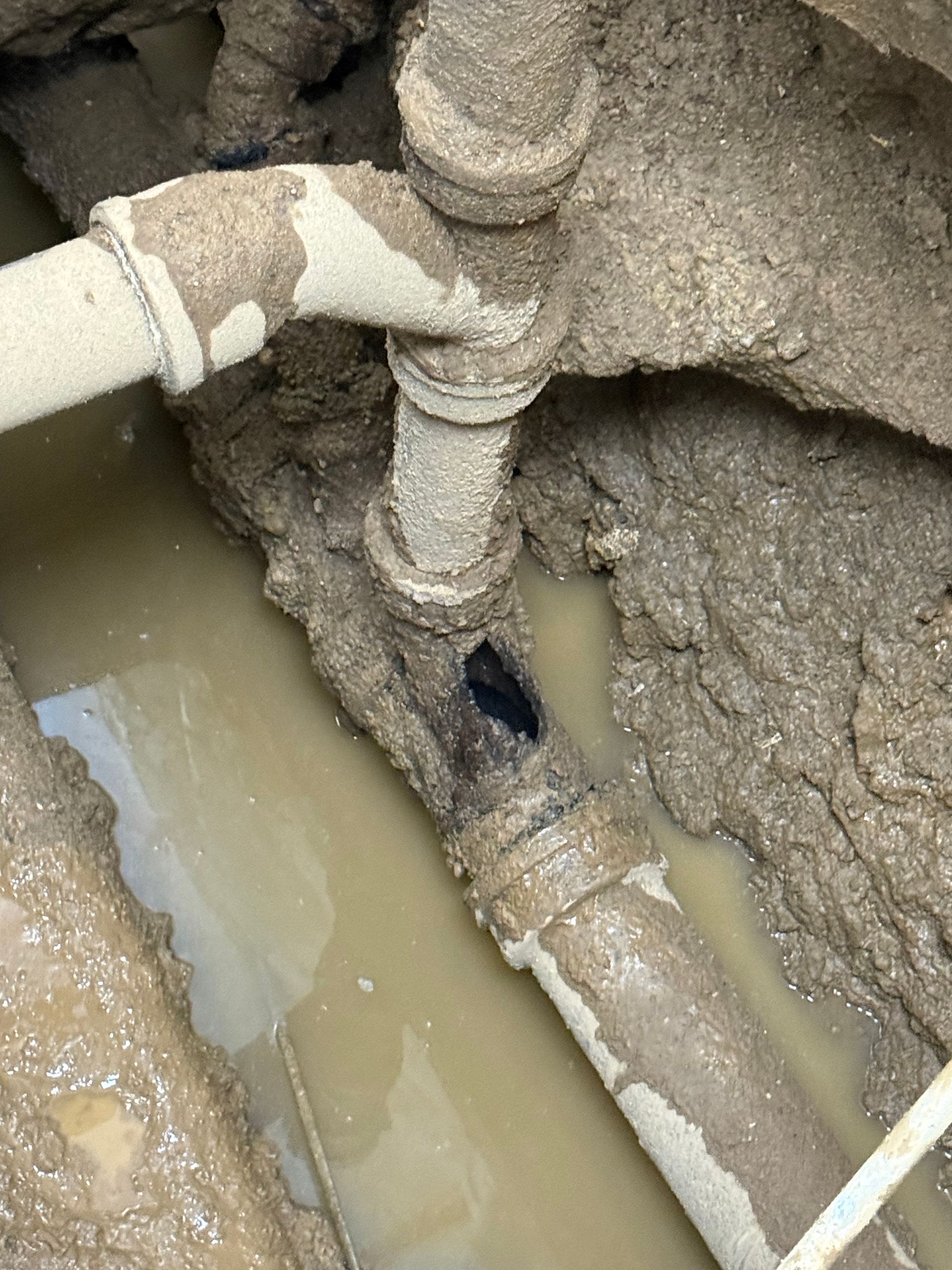 Muddy flooded trench with broken pipes and standing water