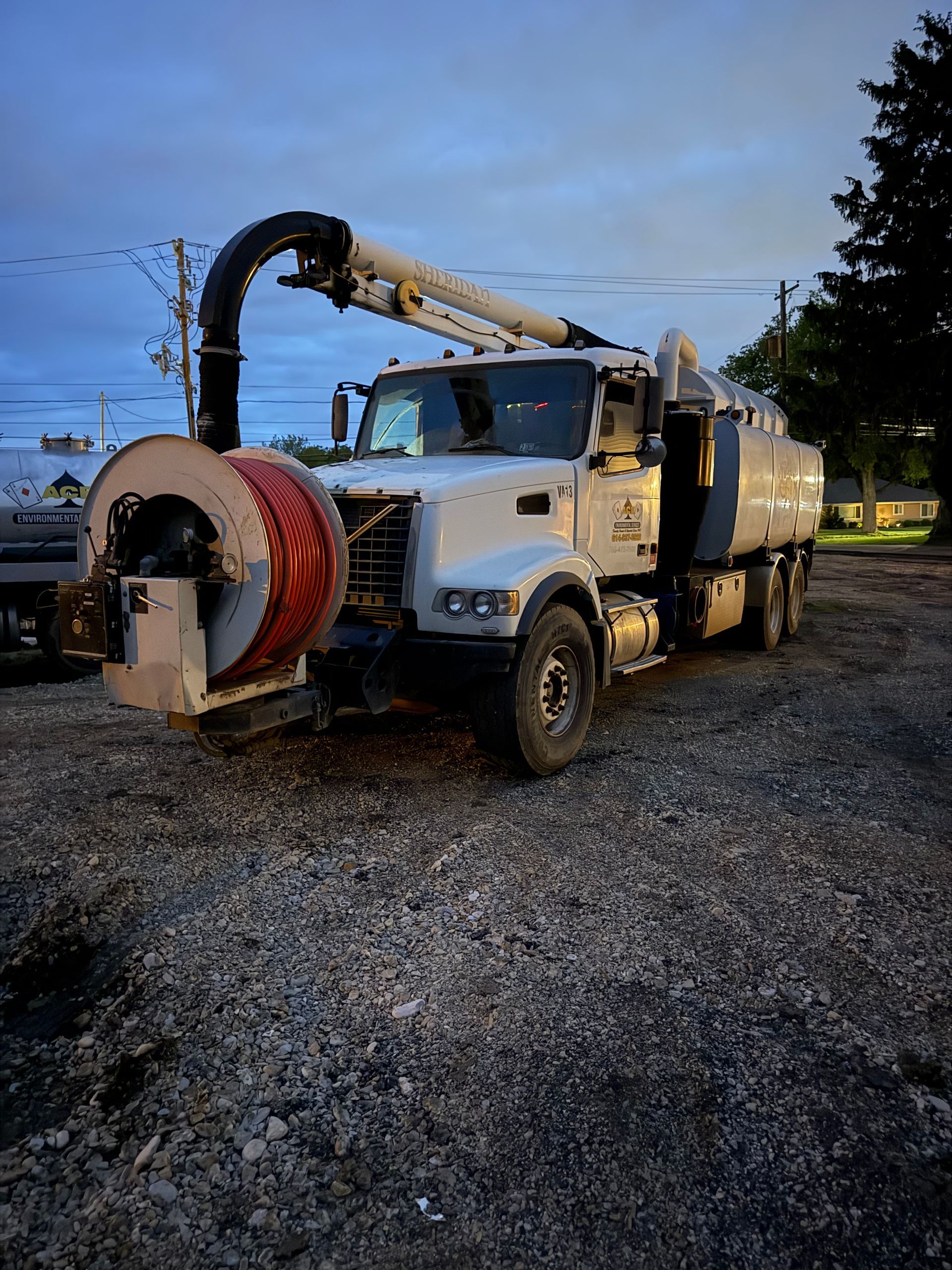 White utility truck with mounted boom and hose reel parked on gravel at dusk