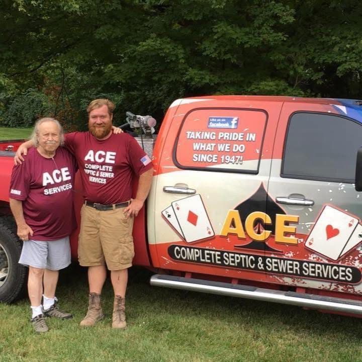 Two people in maroon ACE shirts stand beside an ACE septic and sewer services truck.