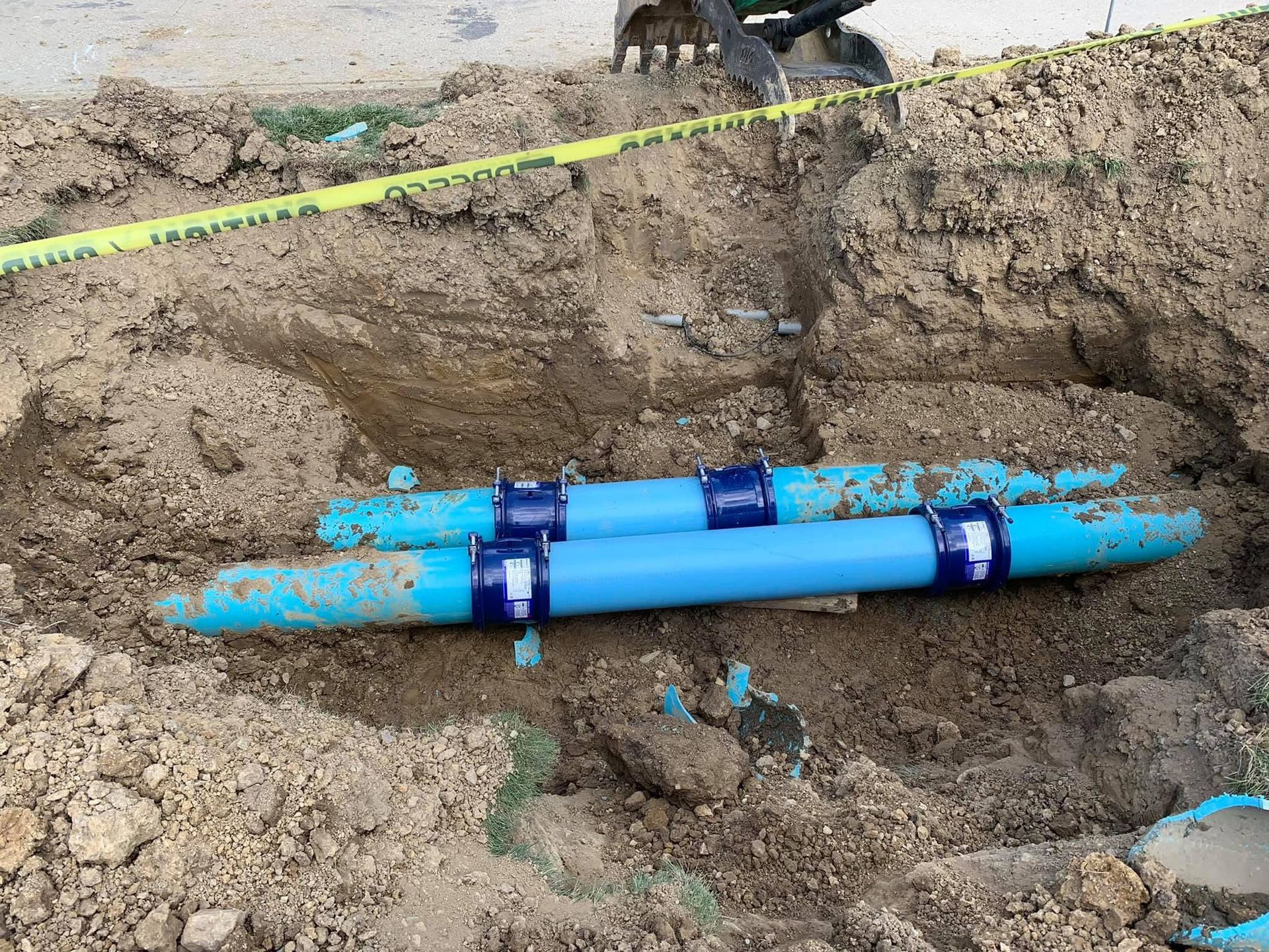 Blue utility pipes in an excavated trench at a construction site, with yellow tape marking the area.