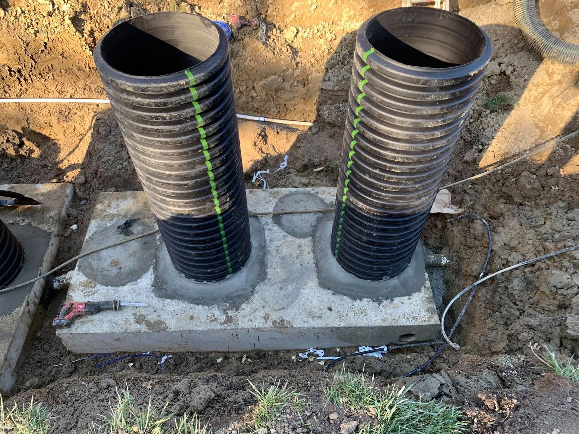 Two black corrugated pipes set in a concrete base at a construction site