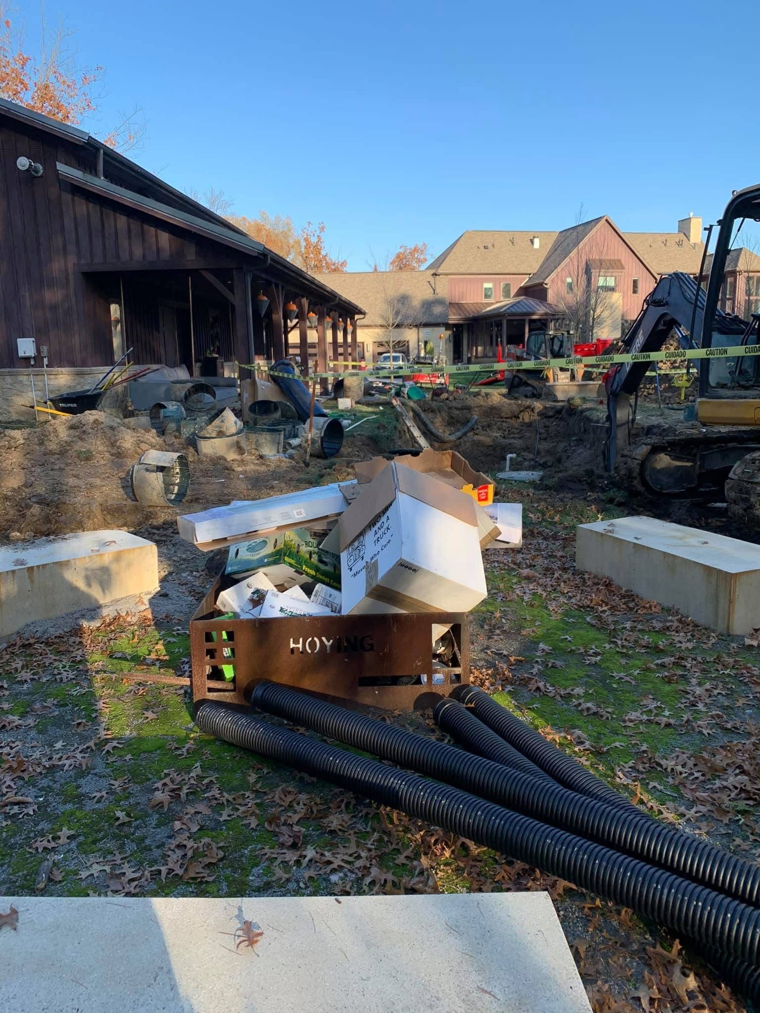 Backyard construction site with debris, pipes, and a large pile of earth beside buildings under clear sky