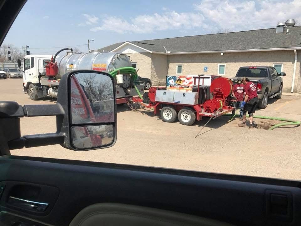 Pickup truck with red farm equipment hitched behind it in a gravel lot under a partly cloudy sky