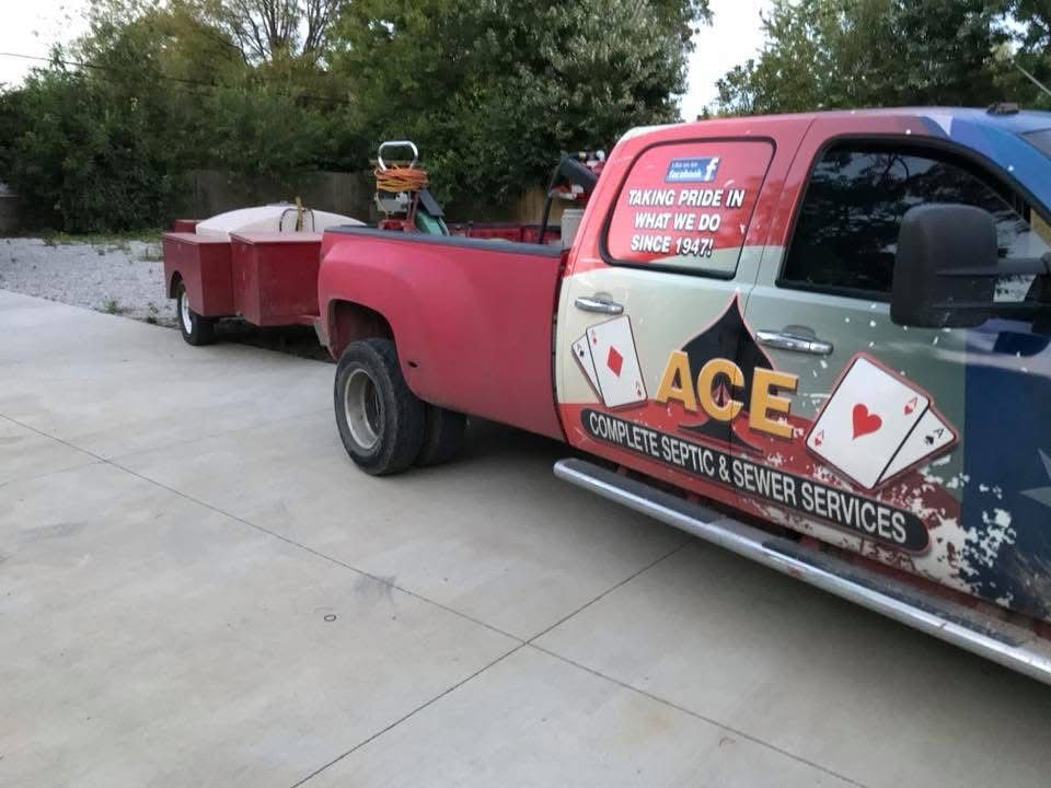 ACE Service Services truck hauling a red trailer on a driveway, with cards graphics on the door.