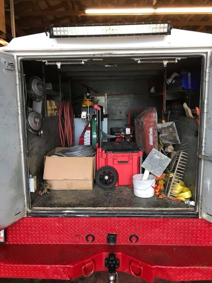Open truck or van cargo area filled with tools, boxes, and equipment, with a red generator in front.