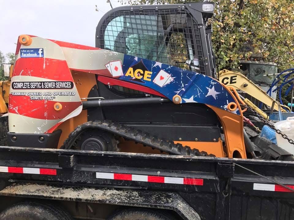 Blue and orange skid steer with ACE branding loaded on a black trailer outdoors