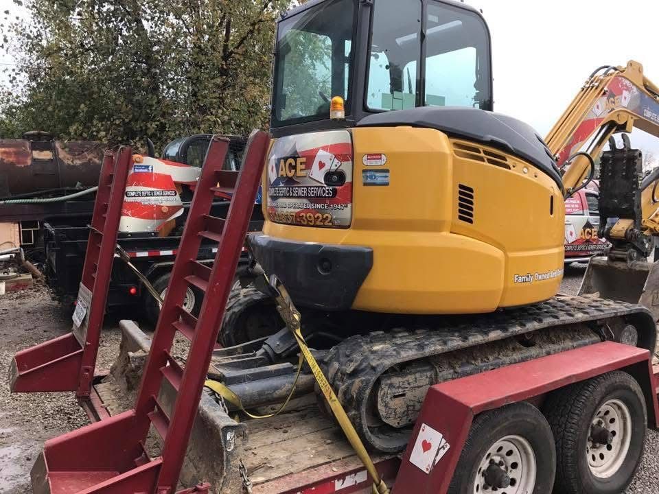 Yellow mini excavator on a red trailer at a construction site, with barriers and another excavator nearby