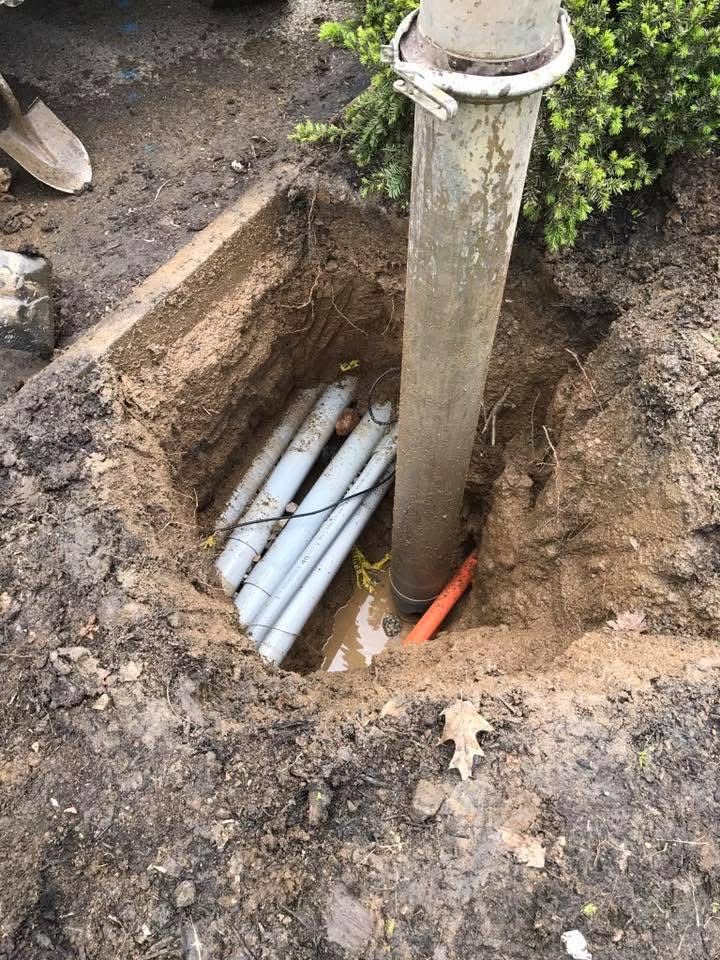 Open trench around a utility pole, with exposed white pipes and an orange cable underground