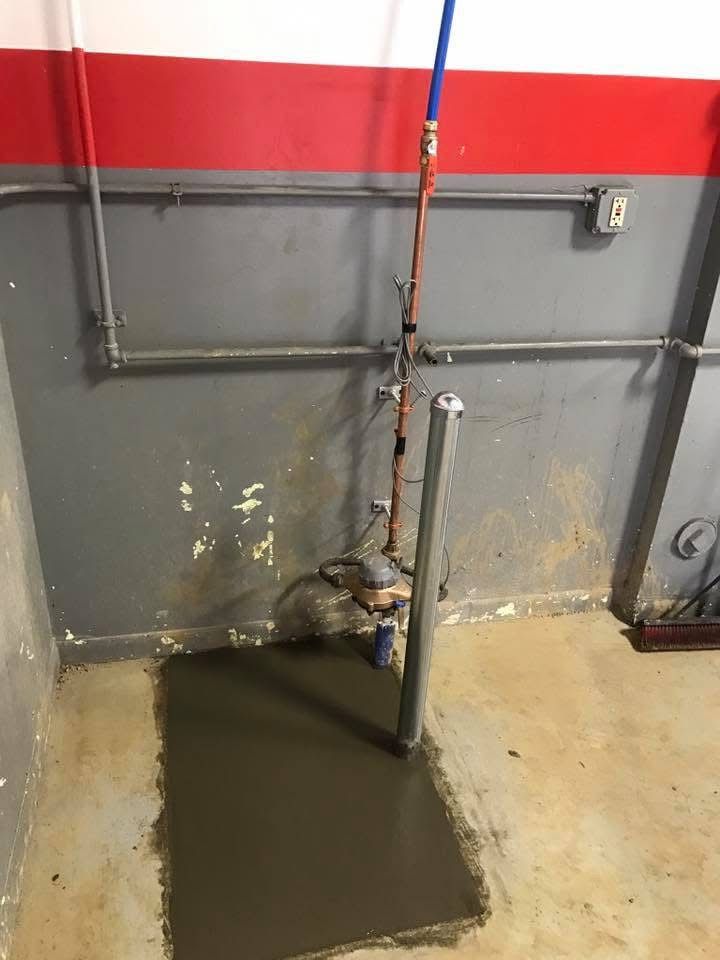 Broken pipe leaking water onto concrete floor in a gray industrial room with a red wall stripe
