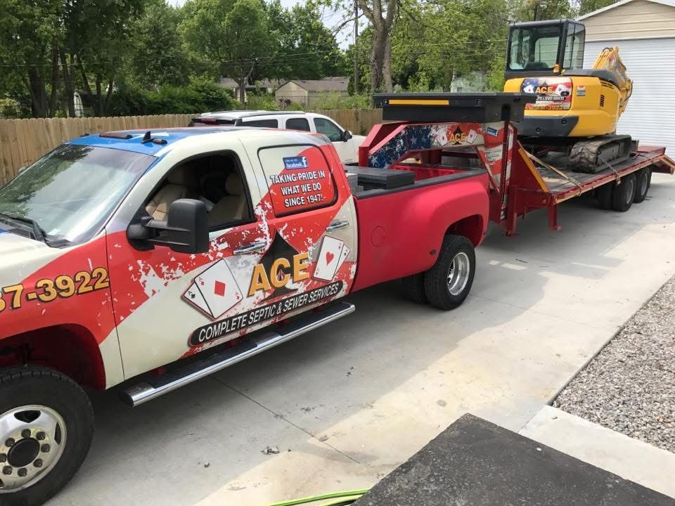 Red tow truck hauling a yellow construction machine on a flatbed trailer by the roadside