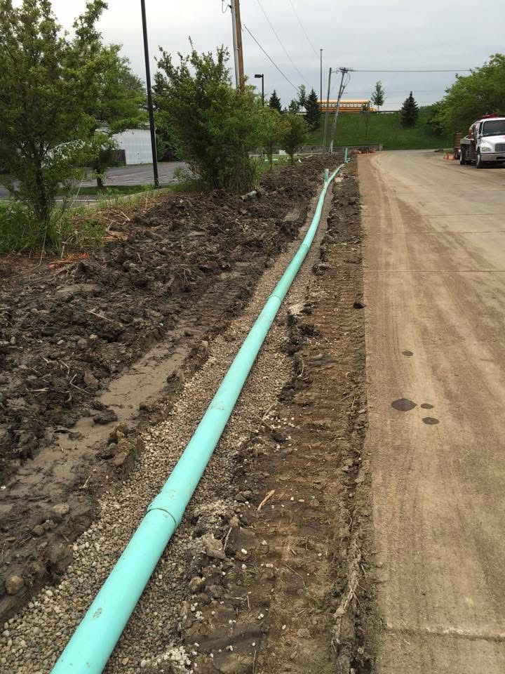 Turquoise pipe laid along a dirt roadside beside a paved lane and trees