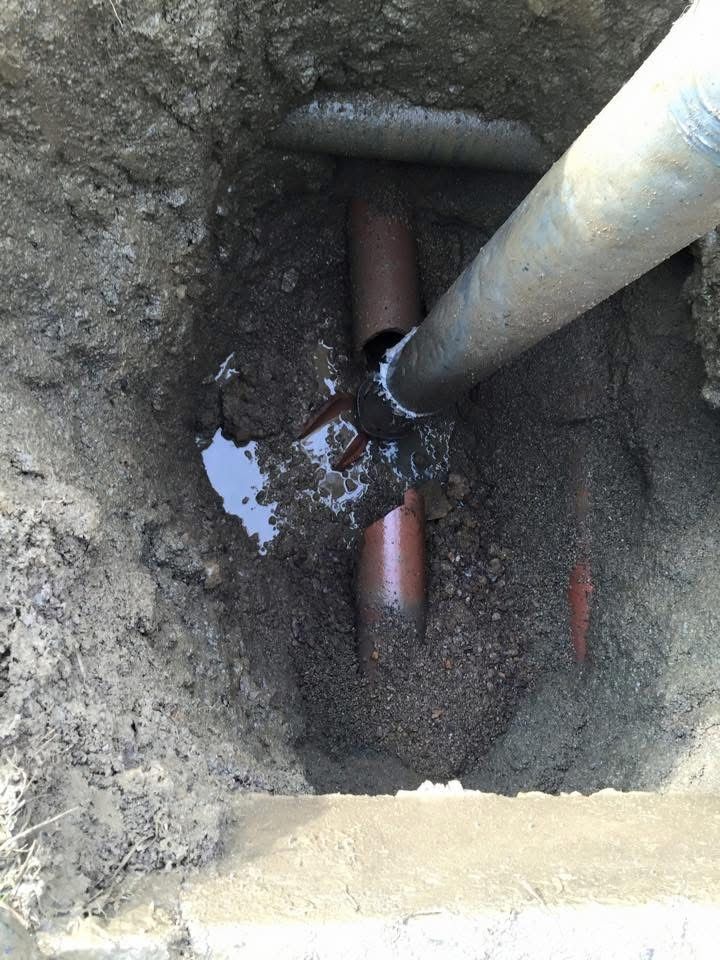 Excavation pit with a copper pipe and a white pipe connected at the bottom, surrounded by muddy soil and water.