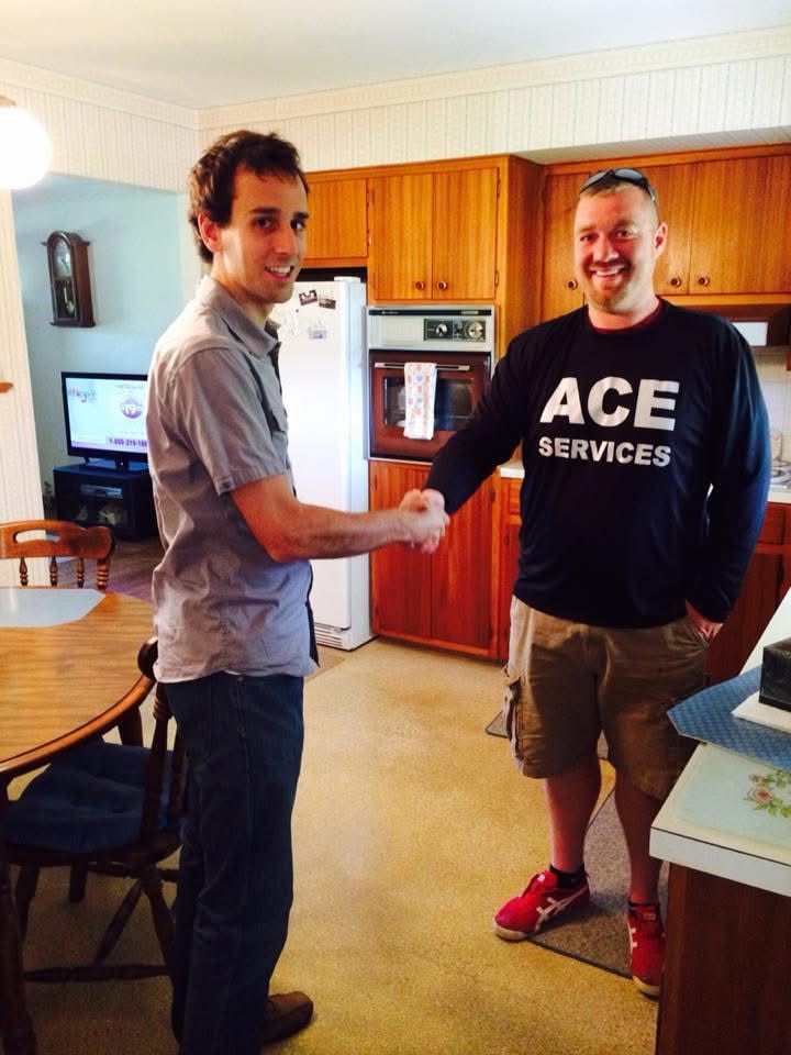Two men shaking hands in a kitchen, one in an ACE Services shirt.