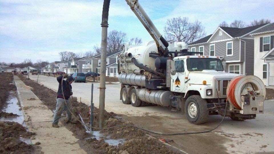 Worker operating a truck-mounted auger beside flooded mud at a suburban construction site
