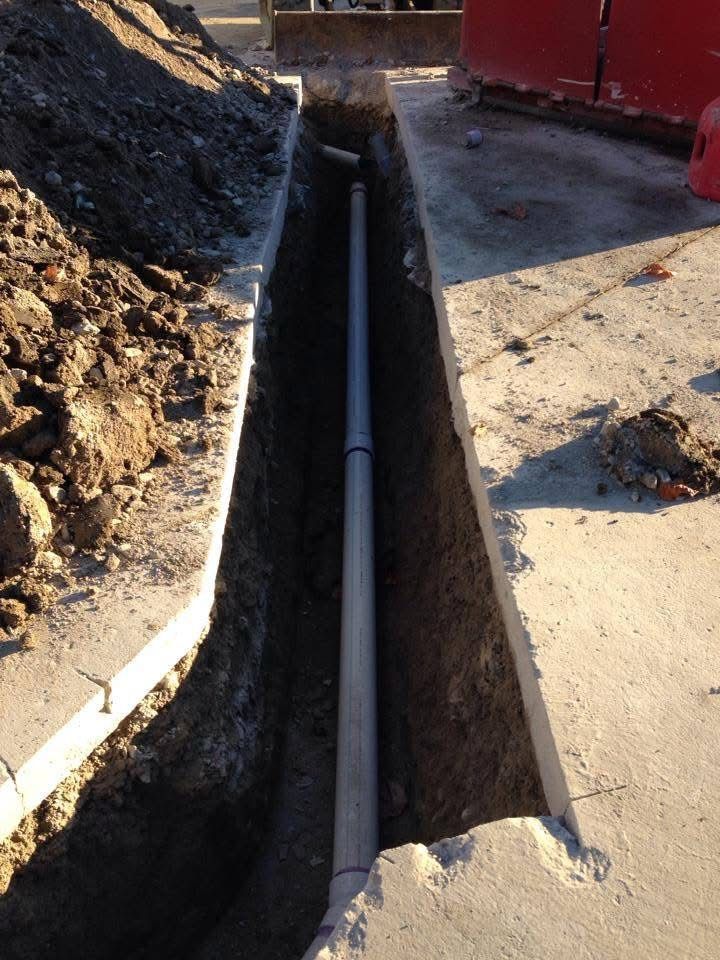 Trenched utility pipe laid in a narrow excavation beside a concrete path during construction.