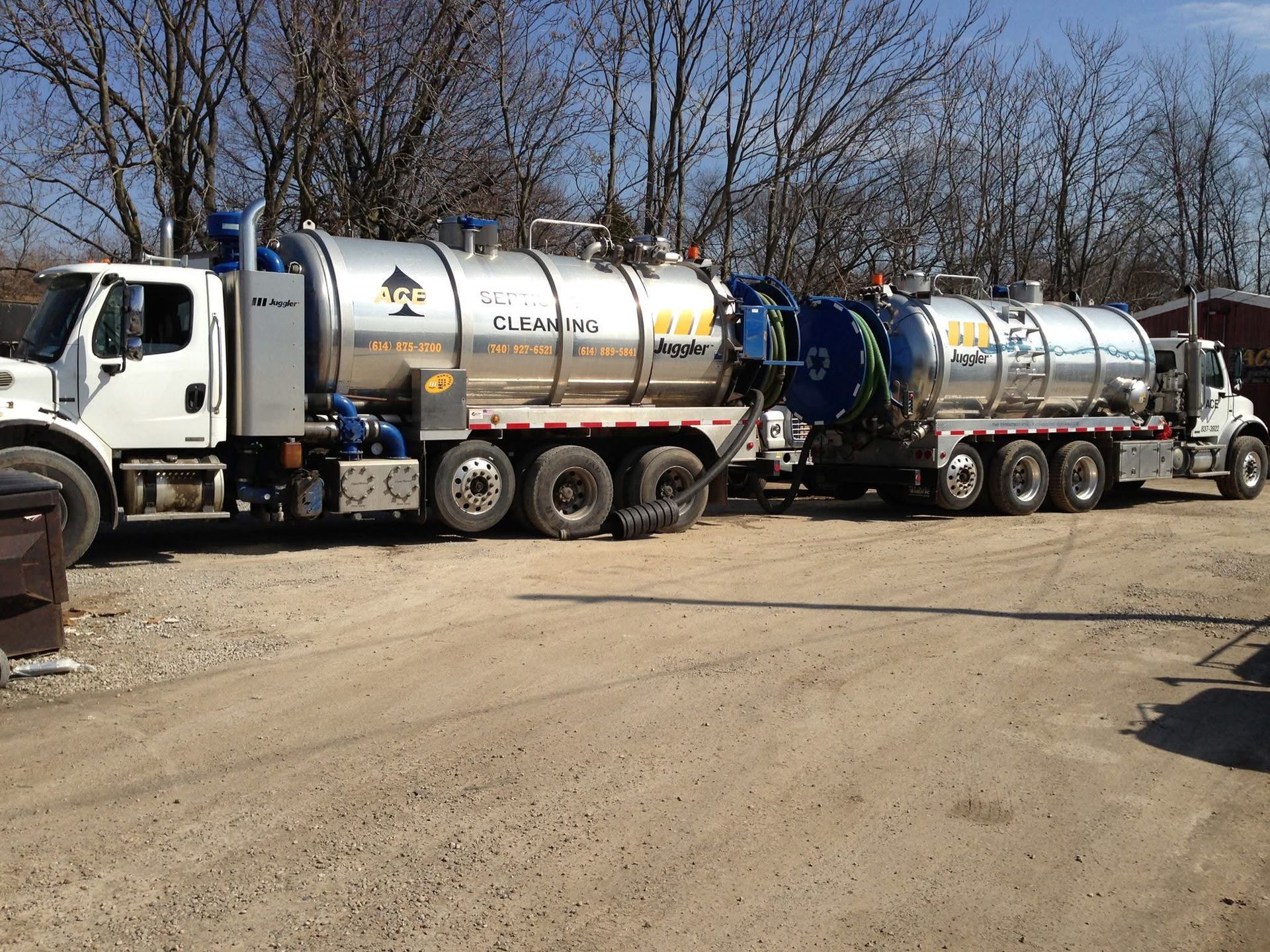 White tanker truck hauling large silver tank trailers on a dirt lot under bare trees