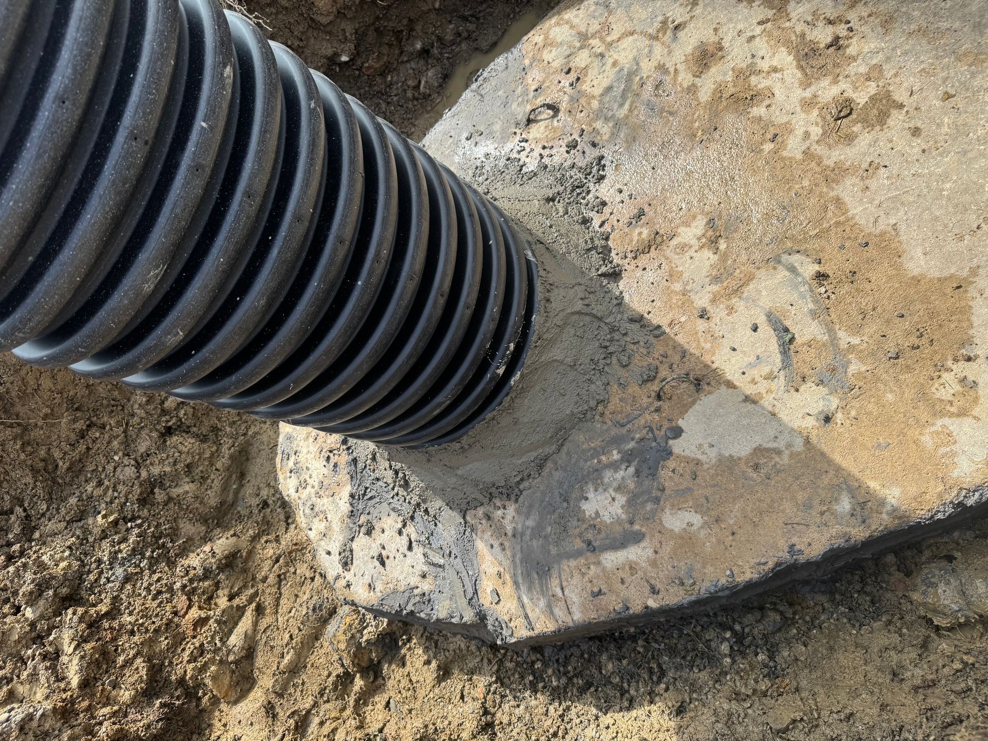 Black corrugated pipe entering a concrete base on dirt ground