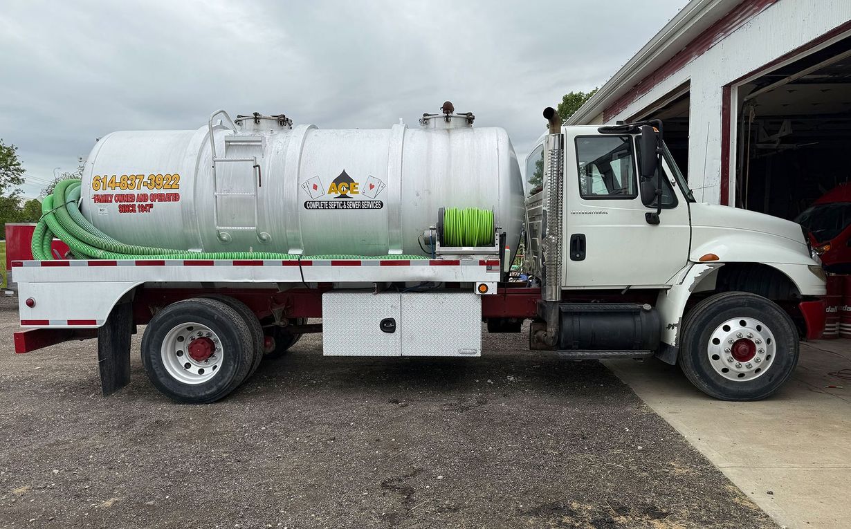 White vacuum truck parked beside a building on a gravel lot, side view