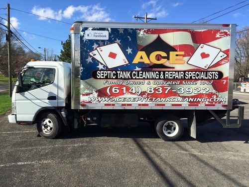 White ACE septic tank service truck with large red, blue, and yellow advertisement on the side, parked outdoors.
