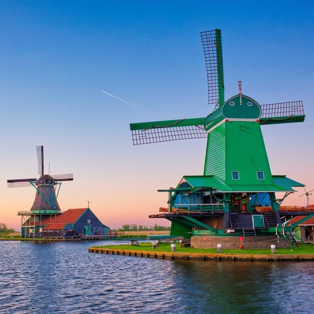 Two green windmills by a calm canal at sunset with a pink-blue sky