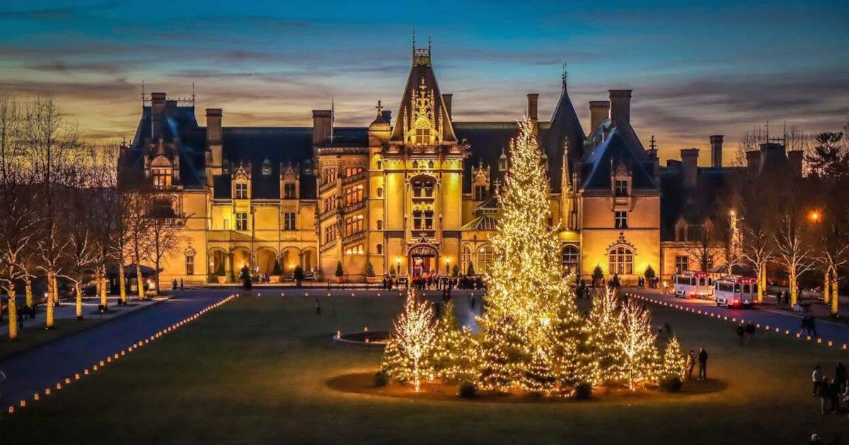 Illuminated historic mansion at dusk with a large lit Christmas tree in the foreground