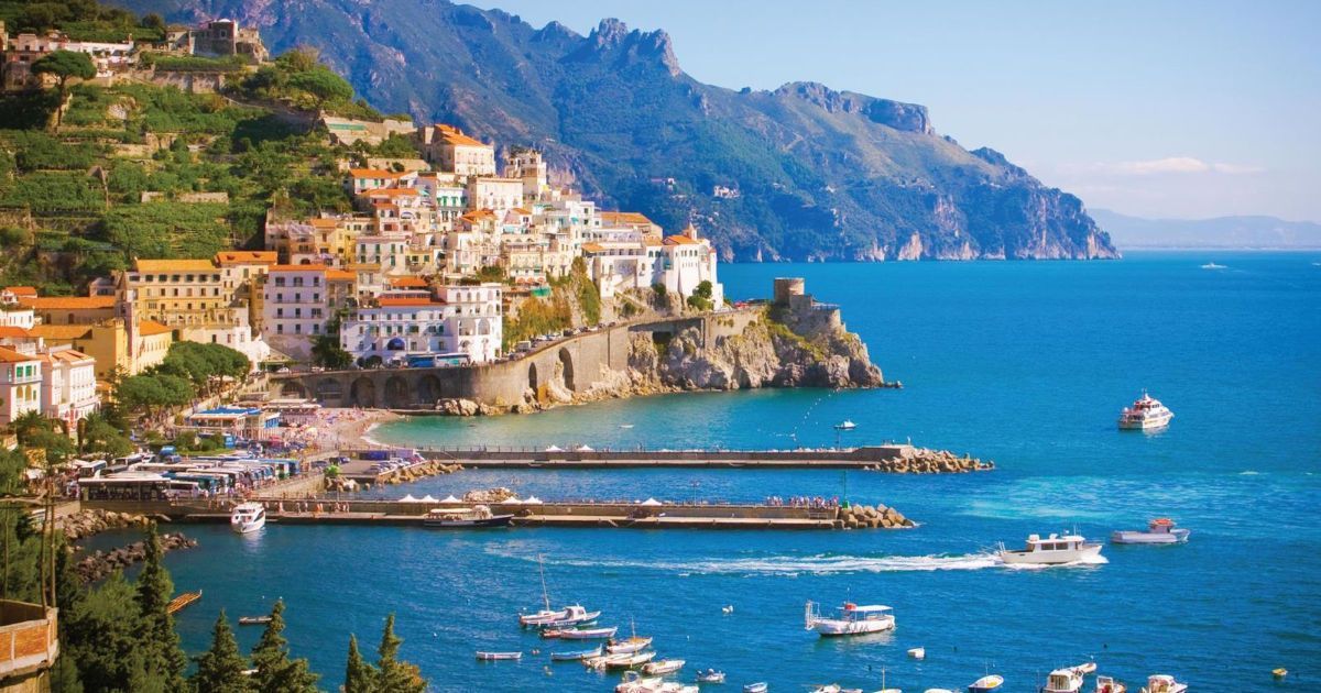 Coastal village with colorful buildings on a rocky hillside beside a blue harbor with boats and a pier