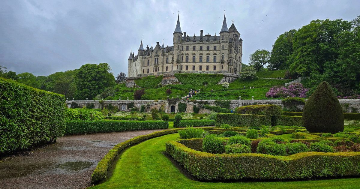 Grand castle above manicured gardens and stone paths under a cloudy sky