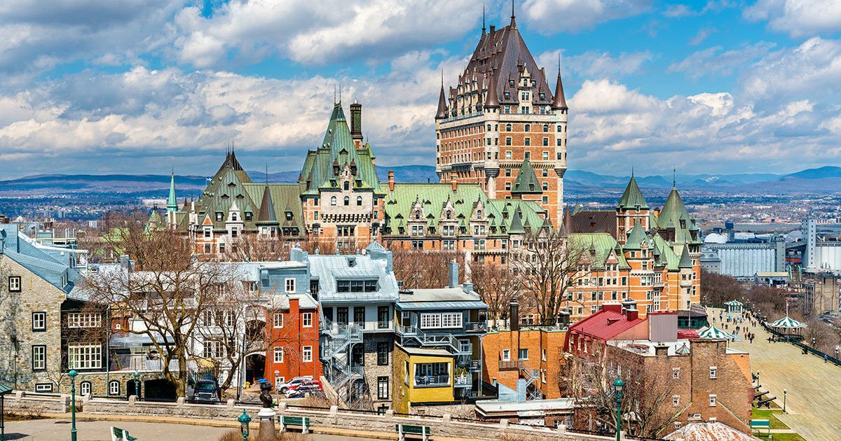 Colorful historic buildings and a tall château overlooking a winter cityscape under cloudy skies