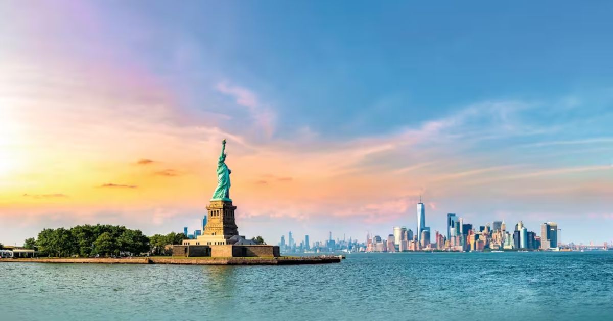 Statue of Liberty at sunset with New York City skyline across the harbor