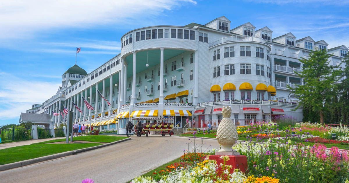 Grand hotel with white balconies and yellow awnings beside a flowered drive under a blue sky