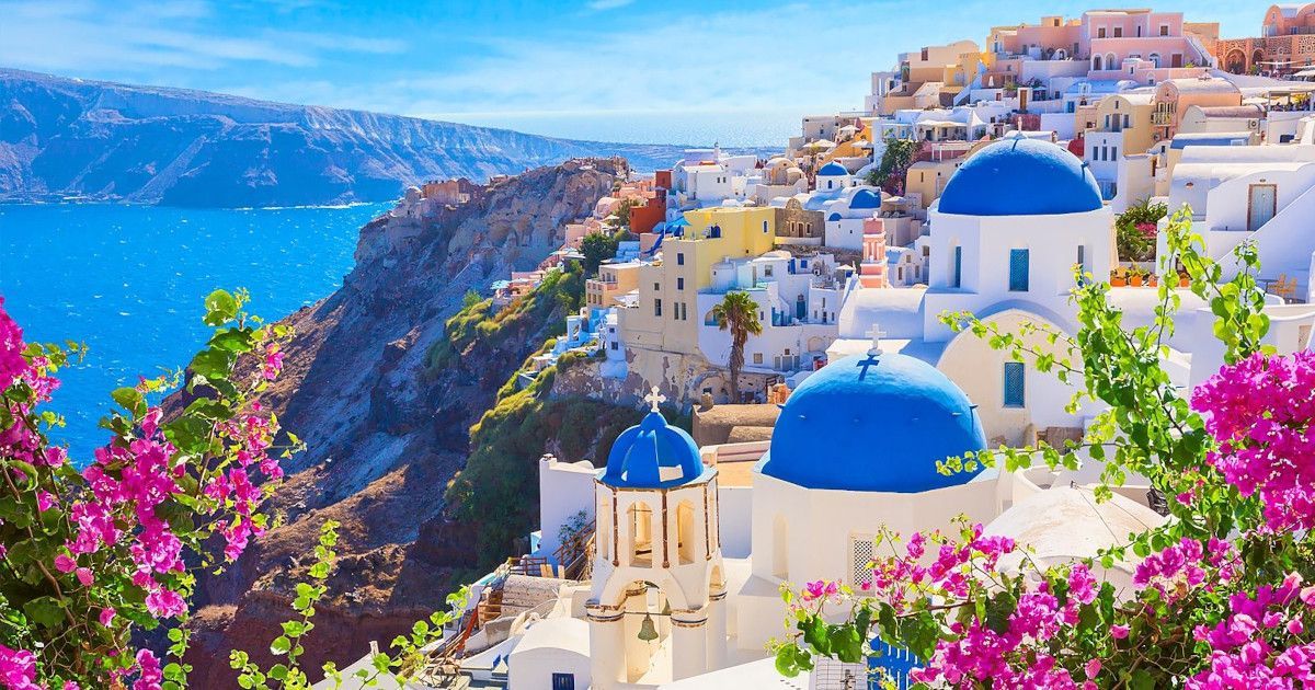 White-and-blue cliffside village overlooking the sea, with bright pink bougainvillea in the foreground.